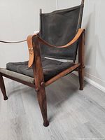 Front right angle view showing wood frame, black canvas seat and back, and leather arm straps