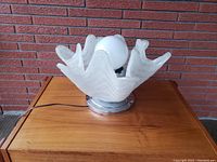 Front left angled view of the vintage table lamp showing wavy frosted white glass shade with marble-like veining and chrome base sitting on wood table against brick wall.