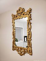 Full view of the gold framed wall mirror mounted on a wall showing the entire frame and reflective surface.