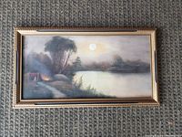 Full view of the antique landscape painting with ornate gold-tone frame showing lakeside, trees, and fire scene.