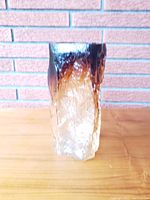 Front view of rectangular abstract art glass vase with dark amber top fading to clear textured glass base against brick background