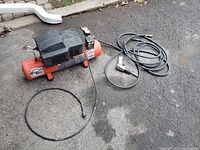 Foto del compresor de aire portátil anaranjado con el cincel neumático y mangueras.