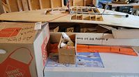 Overview of boxes containing model airplane kit parts including orange wing panels and small hardware box