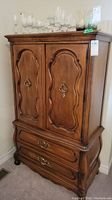 Front view of the wood armoire showing detailed carved doors and drawers with metal handles.