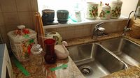 Photo shows items arranged around kitchen double sink including white fruit motif canister, red vase, glass jar with lid, white swan figurine, candles, and assorted planter pots.