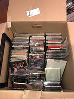 Photo of large cardboard box filled with CDs stacked vertically and horizontally, showing many titles and jewel cases