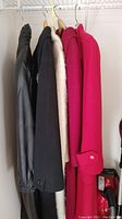 View of four coats hanging on a rack showing different materials and colors including black leather, cream wool, and two pink/red wool coats.