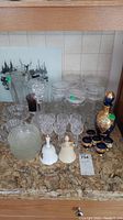 Overview of glassware on countertop including decanter with matching glasses, glass storage jars, aperitif glasses, two decorative bells, and additional glass pieces.