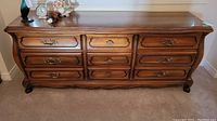 Full front view of the 9 drawer dresser showing decorative drawer fronts and brass handles, curved edges, ball feet, and wood grain finish.