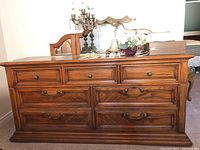 Seven drawer wood dresser front view with decorative metal hardware and wood grain finish, showing overall condition and style.