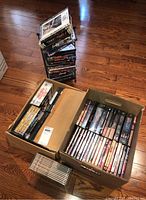 Photo of two full boxes and one metal rack containing over 50 DVDs stacked upright showing titles visible along the spines.