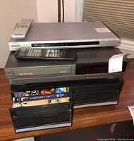 Sharp VC-H870 VHS player with Sony DVD/CD player on top, organizer box below containing VHS tapes.