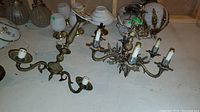 Both chandeliers shown together on table with visible candle-style sockets and brass ornate arms