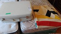 Photo showing the off-white hardcase luggage closed next to the folded wool blanket with colorful geometric design