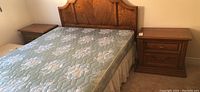 Photo showing one wood night stand next to a bed with a headboard and mattress, illustrating size and style.