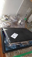 Overall view of tea set items and cutlery box on textured table surface.
