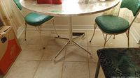 Photo of round vintage table with metal legs and two green vinyl chairs.