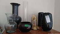 Wide view showing five items: 2 black vases, 1 clear bowl-shaped vase, 1 tall clear cylindrical vase, and gold-tone domed clock.