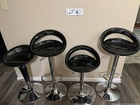 Four adjustable black and silver bar stools, three matching and one slightly different, arranged against wall