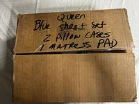 Closed cardboard box labeled with contents: Blue queen sheet set, 2 pillow cases, 1 mattress pad.