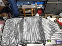 Open suitcase showing the grey and white striped interior with two compartments, securing straps, and zippered divider panel.