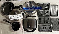 Full overview of the kitchen set items including three frying pans, Dutch oven with lid, metal colander, Farberware Panini maker and six interchangeable grilling trays (two sandwich, two waffle, two grill plates).