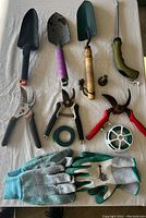 Complete view of garden tools and gloves laid out on white surface.
