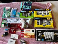 Image of assorted light bulbs and lamps on pink towel, showing multiple brands and types including LED, incandescent, and specialty bulbs.