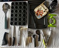 Photo showing various bakeware and kitchen utensils including muffin pan, baking sheets, spatula, pot holder, and green apple slicer.