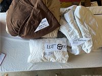 Comforter folded showing brown and tan reversible sides, mattress pad and fitted sheet folded on white surface with handwritten labels
