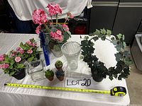 Full view of all items on white cloth surface with measuring tape showing size, including silk flowers, artificial succulents, ivy wreath, and two glass vases.