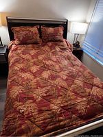 Queen bed made up with Tommy Bahama comforter and matching pillows, showing tropical leaf pattern in warm rust and beige colors.