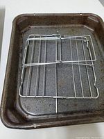 Rectangular, heavily used dark metal roasting pan with a flat metal rack laid inside.