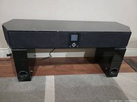 Front view of gloss black electronic table with integrated speakers and control panel