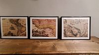 Three framed vintage style maps arranged side by side on wooden surface against a plain wall.