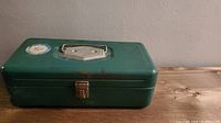 Closed green metal box with silver handle and latch, showing front and top.