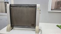 Front view of the electric room heater showing the black metal mesh grill, white plastic sides with scratches, and cream-colored feet