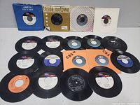 Overhead photo showing 17 black vinyl 45 RPM records, some in paper sleeves including Tamla Motown, CBS, and Ampex labels. Records are scratched and vintage.
