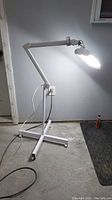 Full view of the magnifier lamp illuminated, showing adjustable multi-jointed arm and four-legged rolling base with casters.