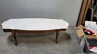 Full view of the coffee table showing the white marble top and wooden frame with curved legs.