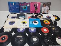 Overview photo of about 20 vinyl 45 RPM records arranged with covers and record labels visible showing condition and variety of records.