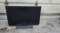 Full view of Philips TV showing screen, frame, and attached stand sitting on a concrete floor, power cord nearby.