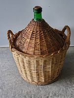 Full view of the large green glass wine bottle inside the woven wicker basket with side handles