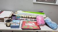 Photo showing multiple holiday-themed wrapping paper rolls, ribbons, and gift bags spread on a table.