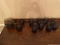 23 pieces of blue and brown tinted glass dishware including bowls and cups arranged on a wooden table.