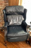 Front angle view of a blue leather recliner chair showing the padded backrest, seat, nailhead trim on armrests, and curved wooden legs with claw feet.