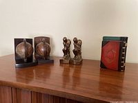 Three different pairs of bookends, including globe bookends, figurine bookends, and decorative book-like bookends on wooden surface.
