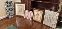 All 5 Christian art pieces arranged on a wooden floor leaning against wooden furniture. Includes sketches, quotes, and a hand-stitched fabric item.
