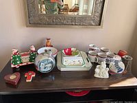 Full view of wood shelf with Christmas mugs, salt and pepper shakers shaped like Christmas trees, ceramic platters with holiday designs, heart-shaped box, cross-shaped ornament, and polar bear figurines.