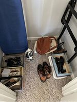Wide shot showing the shoes, purses, iron, and part of the ironing board in a corner on carpet.